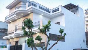 Une maison moderne à deux étages, dotée d’un balcon, avec une voiture garée devant et un arbre dans le jardin.