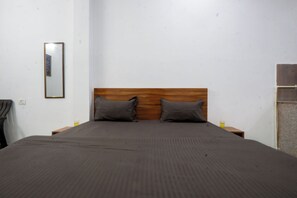 A neatly made bed with a wooden headboard, two pillows, and a gray bedspread in a simple room with white walls and minimal furnishings. - Spacious 6-bedroom building in marvelous Dehradun with AC (Dehradun)