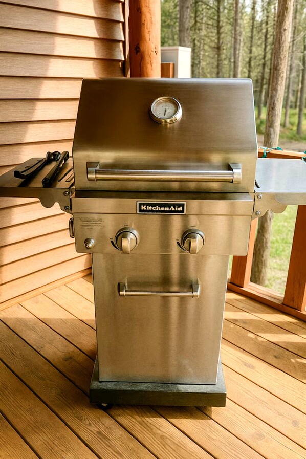 A stainless steel outdoor grill with a digital thermometer, a side burner, and a control knob, placed on a wooden deck.