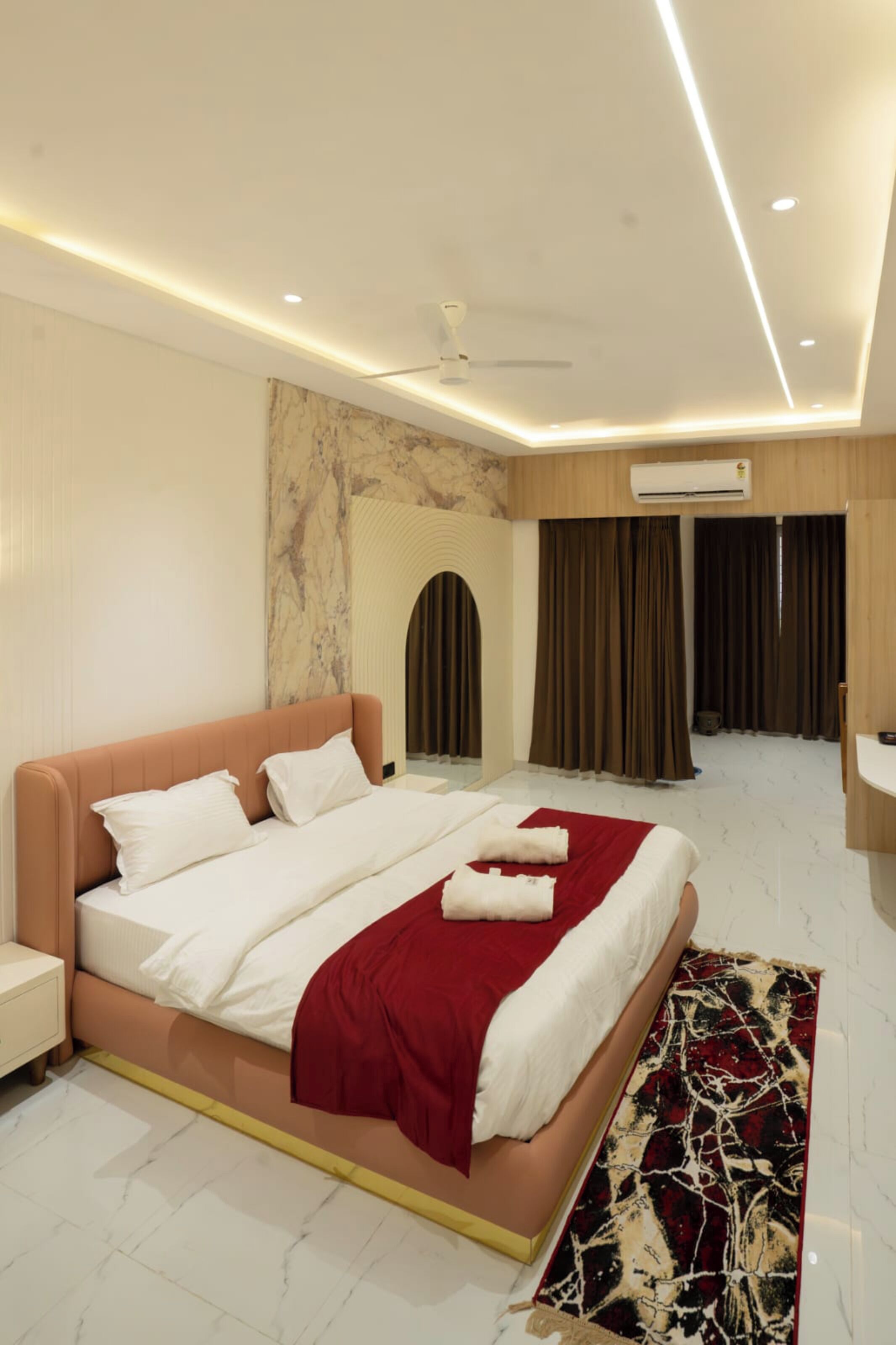 A modern hotel room with a large bed, a marble accent wall, and a ceiling fan.