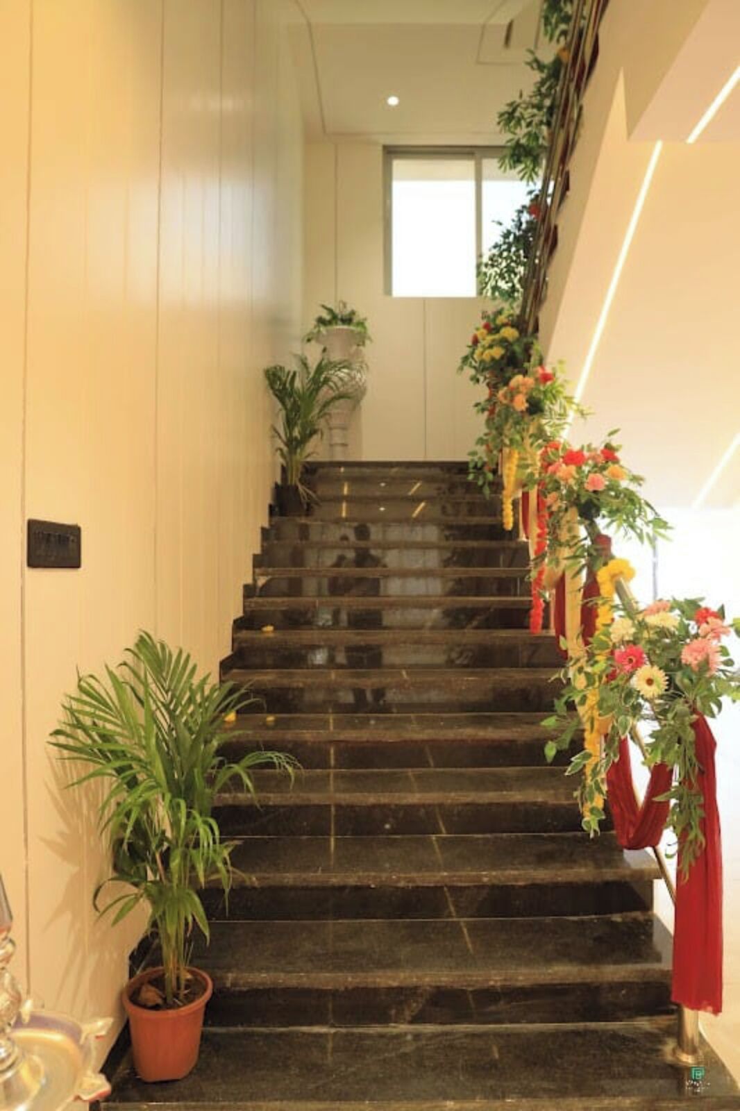 Un escalier orné d’un arrangement floral sur le côté droit et de plantes en pot sur le côté gauche.