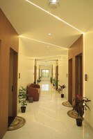 Un pasillo de hotel con diseño moderno, que presenta suelo de mármol, puertas de madera y plantas en macetas a lo largo de las paredes.
