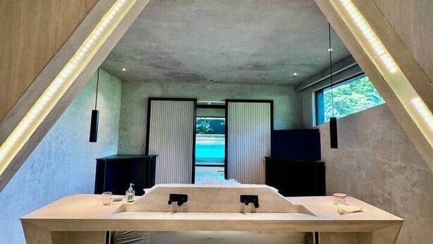 Ein modernes Badezimmer mit einem großen Waschbecken, zwei schwarzen Lautsprechern und Meerblick durch ein Fenster.