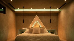Ein modernes Schlafzimmer mit einem zentral platzierten Bett, Nachttischen und einer einzigartigen, dreieckigen Leuchte darüber.
