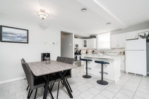 A modern kitchen with white cabinets, a central island with bar stools, a coffee machine, and a view of the dining area.