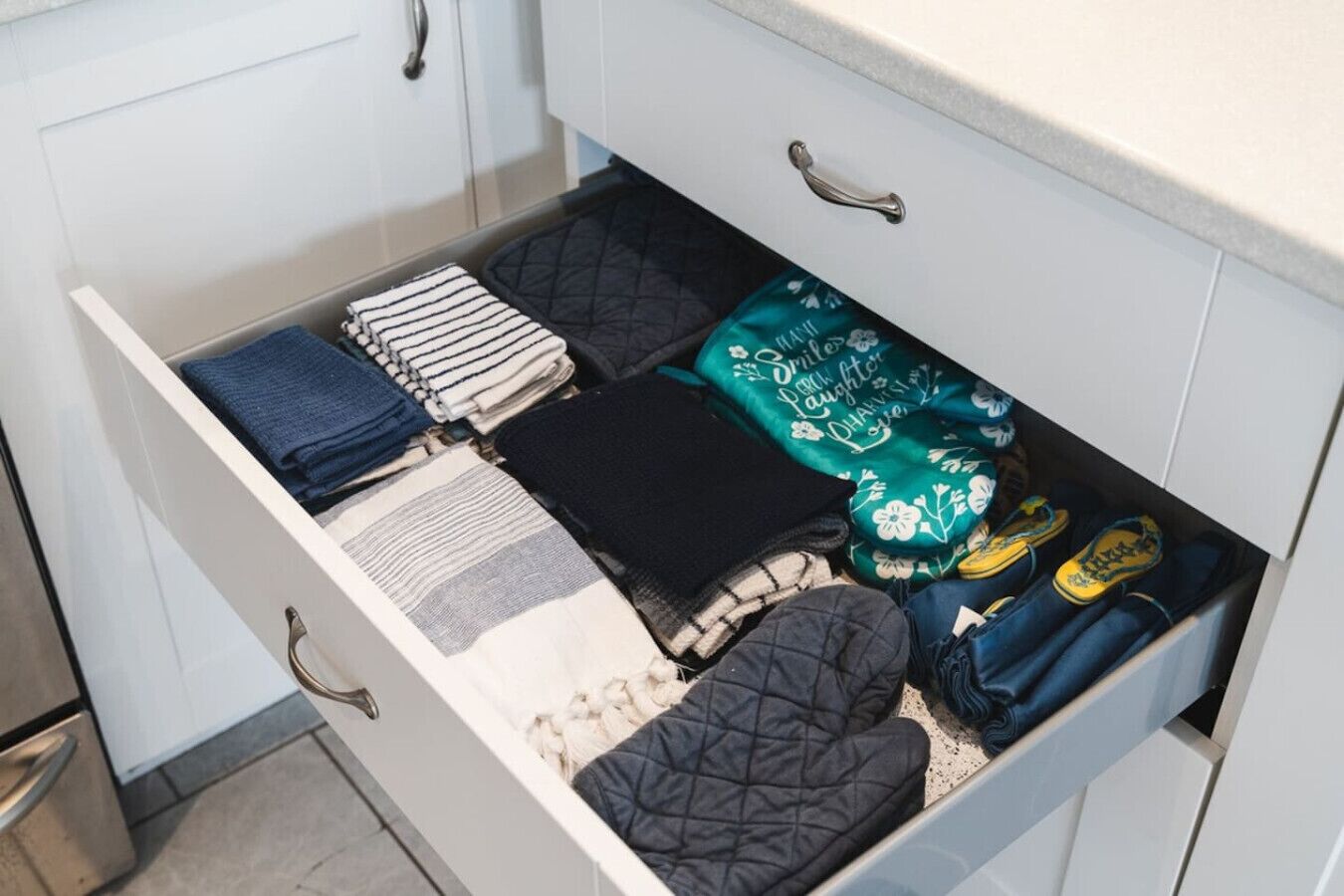Eine Schublade mit ordentlich zusammengelegten Kleidungsstücken, darunter ein grünes, gemustertes Teil und ein blaues.