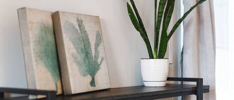 A black metal shelf with two framed botanical prints and a potted plant with long, slender leaves.
