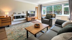 A living room with a sofa, a television, a fireplace, a wooden coffee table, and a large window with curtains.