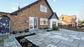 A brick house with a tiled patio, a front door, and a small garden area.