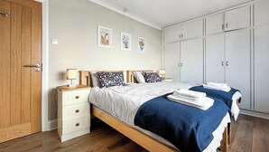 A bedroom with two beds, wooden wardrobe, white walls, and artwork.