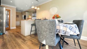 A dining area with a table set for two, a kitchen in the background, and a wooden floor.