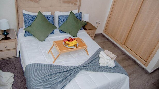 Un lit bien fait, avec un plateau de fruits, des oreillers et une couverture.