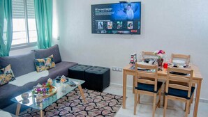 Un salon comprenant un canapé, un pouf, une table basse en verre et un téléviseur fixé au mur, qui affiche l’interface de Netflix.