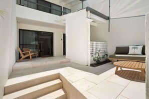 A modern outdoor patio with a wooden bench, a chair, and a staircase leading to a covered area. - Ray St Retreat - Luxury Stay near Sunshine Beach (Sunshine Beach)