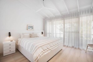 A bedroom with a bed, bedside tables, a nightstand, a chair, and a window with sheer curtains. - Ray St Retreat - Luxury Stay near Sunshine Beach (Sunshine Beach)