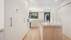 Eine moderne Küche mit weißen Schränken, einer Kücheninsel mit Holzbeschlag und einem Fenster mit Blick auf Grünflächen.