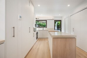 A modern kitchen with white cabinetry, a wooden countertop island, and a window with a view of greenery. - Ray St Retreat - Luxury Stay near Sunshine Beach (Sunshine Beach)