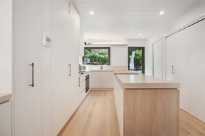 A modern kitchen with white cabinetry, a wooden countertop island, and a window with a view of greenery. - Ray St Retreat - Luxury Stay near Sunshine Beach (Sunshine Beach)