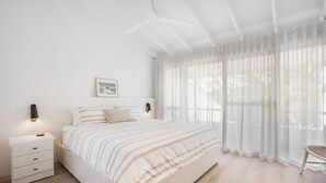 Ein Schlafzimmer mit einem großen Bett, einem Nachttisch mit Schubladen, einer Wandleuchte und transparenten Vorhängen.