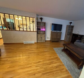 A spacious living room with hardwood flooring, a large TV, and wooden furniture.