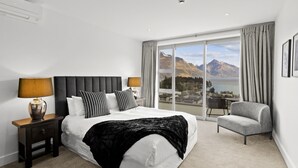 Una moderna camera d'hotel con un letto grande, due comodini, una sedia e vista sulle montagne e un lago.