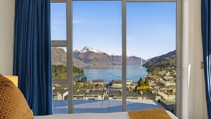 A hotel room with a large window offering a view of a lake, mountains, and a town. - catalina-apt-6-central-penthouse-apt-lake-views (Queenstown)
