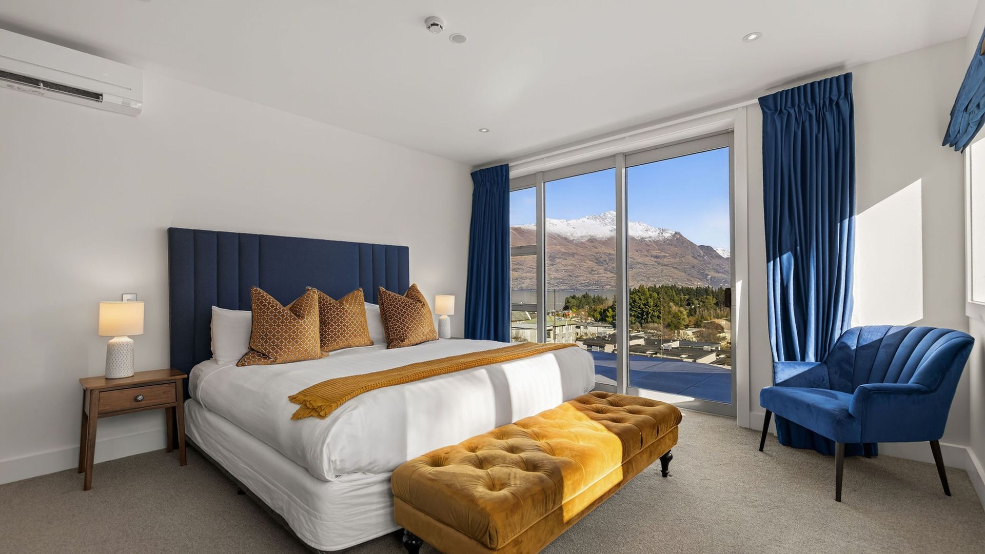 A hotel room with a large bed, a blue chair, and a view of mountains.