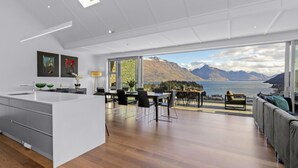 Una cucina moderna con una grande isola, zona pranzo con sedie e vista sulle montagne e su un lago.