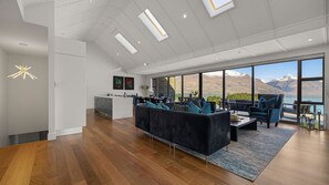 A spacious living area with a large sofa, a dining table, and a view of mountains through large windows. - catalina-apt-6-central-penthouse-apt-lake-views (Queenstown)
