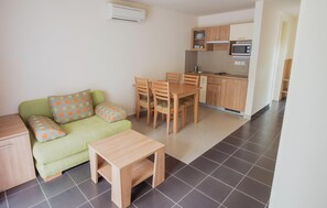 A compact living space with a green sofa, matching cushions, a wooden dining table, and a kitchenette with cabinets and a microwave. - 1 bedroom lovely apartment in Kukljica (Kukljica)