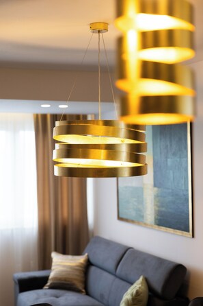 Ein moderner Kronleuchter mit zylindrischer Form, ein graues Sofa mit Kissen und ein Bild an der Wand.