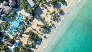 An aerial view of a beachside resort with a swimming pool, palm trees, and beach umbrellas. - Couples Negril - Adults Only (Negril)