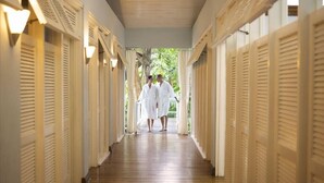 A corridor with wooden flooring and white doors with shutters, leading to an outdoor area with greenery. - Couples Negril - Adults Only (Negril)