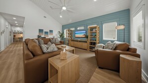 A spacious living room with a large brown leather sofa, a wooden coffee table, and a television on a wooden stand. - Private Pool + Putting Green + Golf Cart Zone + Walk to Beach | Yahwaves (Port Aransas)