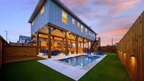 A two-story house with a covered patio, a swimming pool, and a fenced backyard. - Private Pool + Putting Green + Golf Cart Zone + Walk to Beach | Yahwaves (Port Aransas)