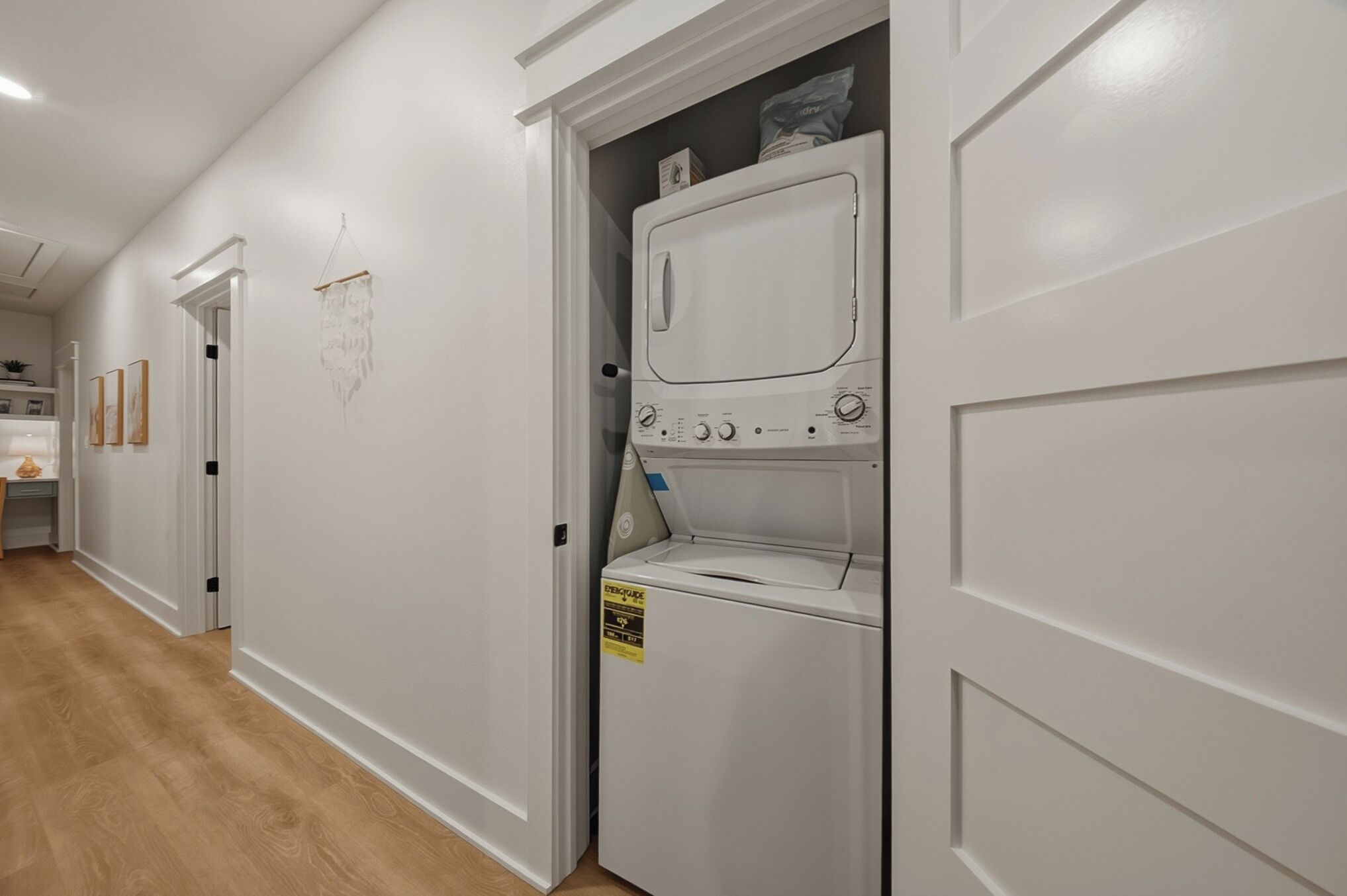 A laundry room with a front-loading washer and dryer, wooden flooring, and a white door.