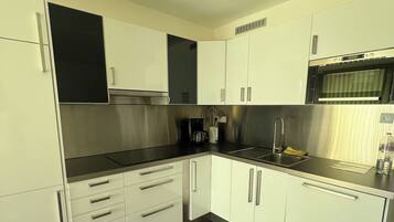 Una cuina moderna amb armaris blancs, una cuina de treball de stainless steel i un forn integrat.