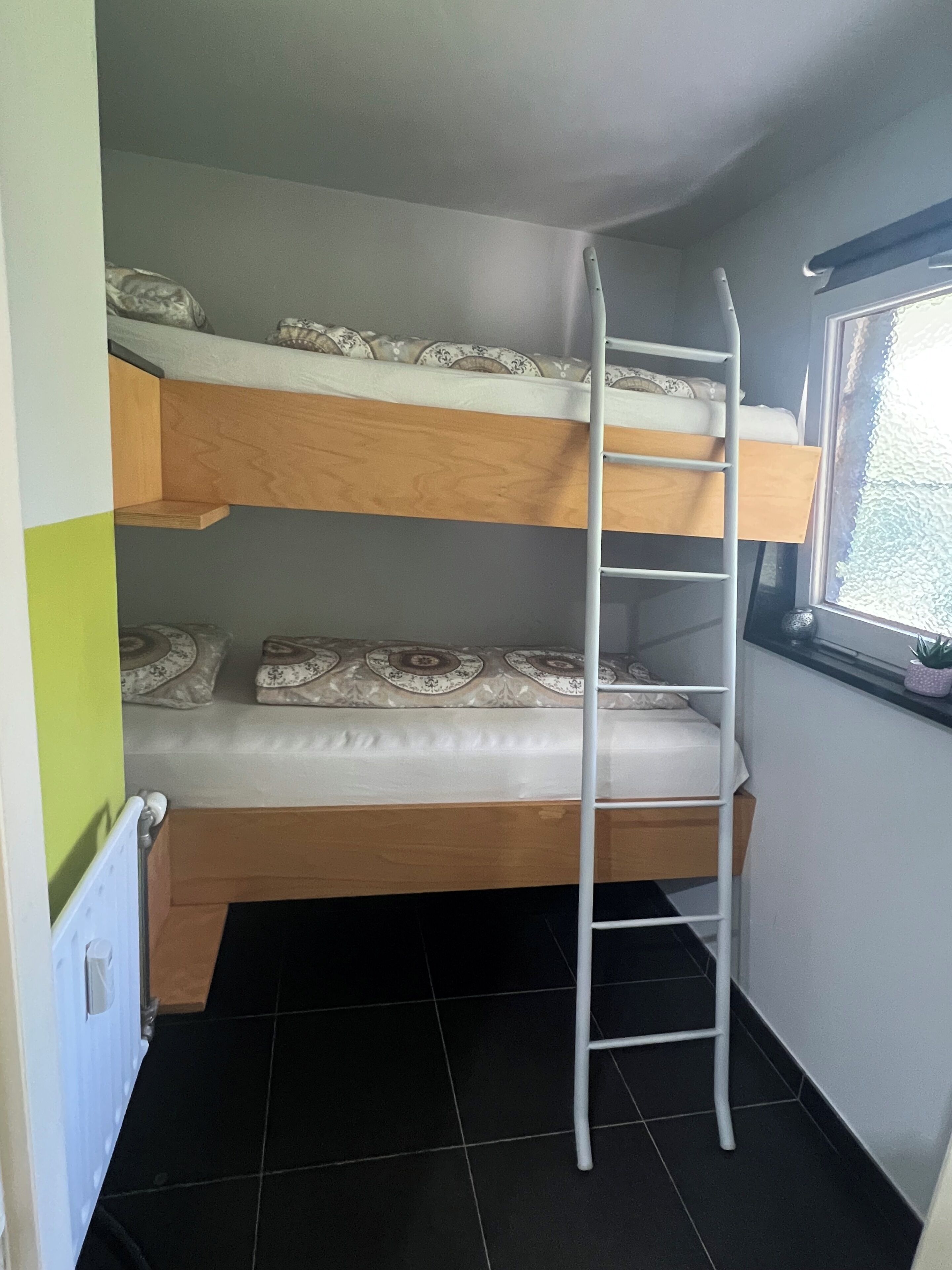 A bunk bed with a ladder, a window with a view, and a radiator.