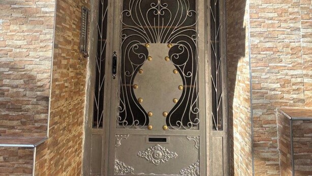 A door with intricate metalwork and a decorative panel, set in a stone wall.