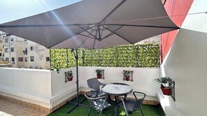 A small outdoor patio with a table and chairs, a large umbrella, and potted plants.