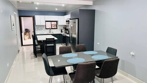 Una cocina moderna con armarios blancos, un refrigerador de acero inoxidable y un comedor con mesa y sillas.