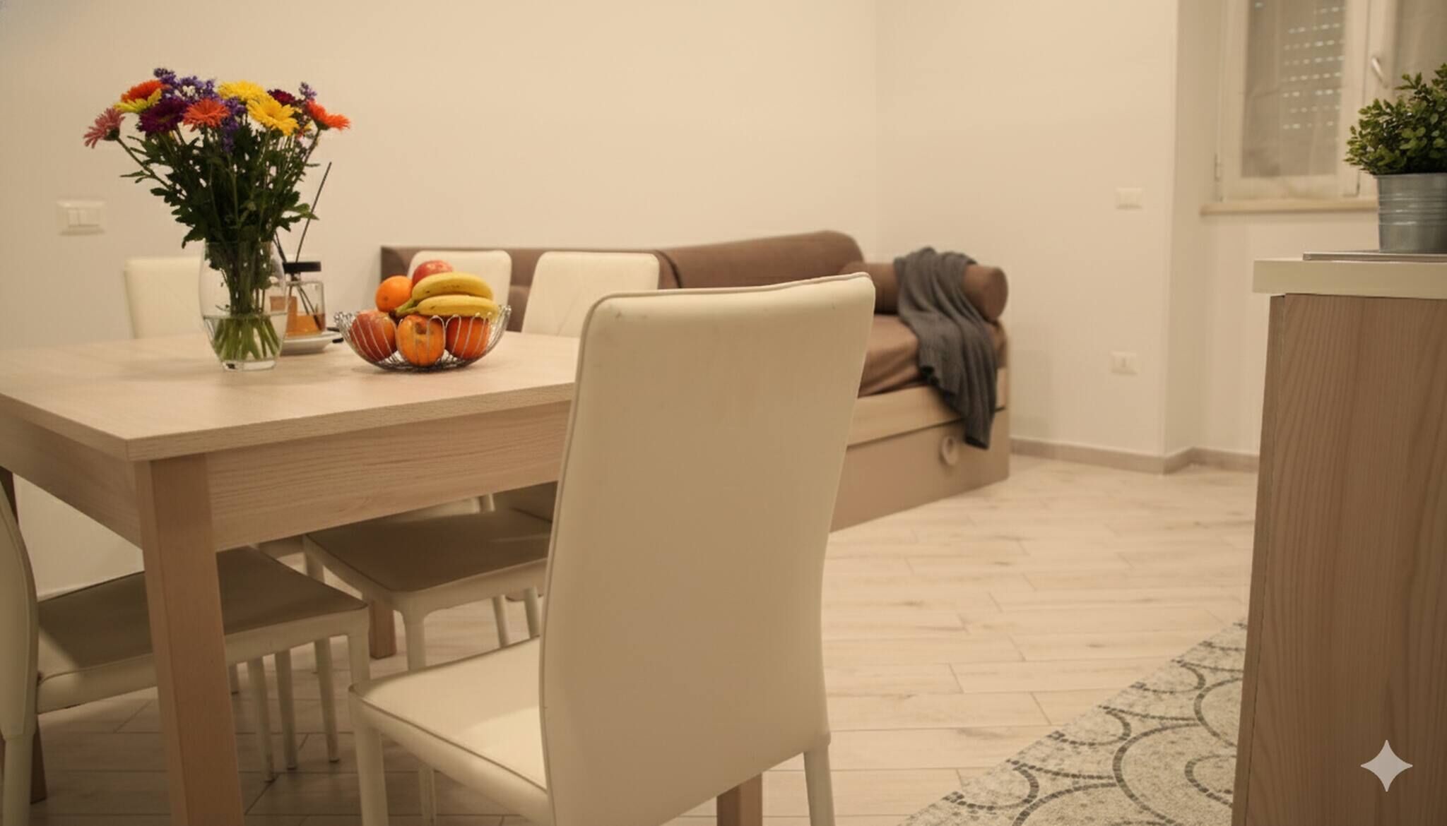 A modern dining area with a wooden table, a vase of flowers, and a fruit bowl.