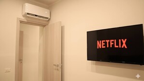 A room with a mounted television displaying the Netflix logo, a door, and an air conditioning unit above the door. - A due passi dagli Scavi con parcheggio gratuito e Wi-Fi (Pompei)