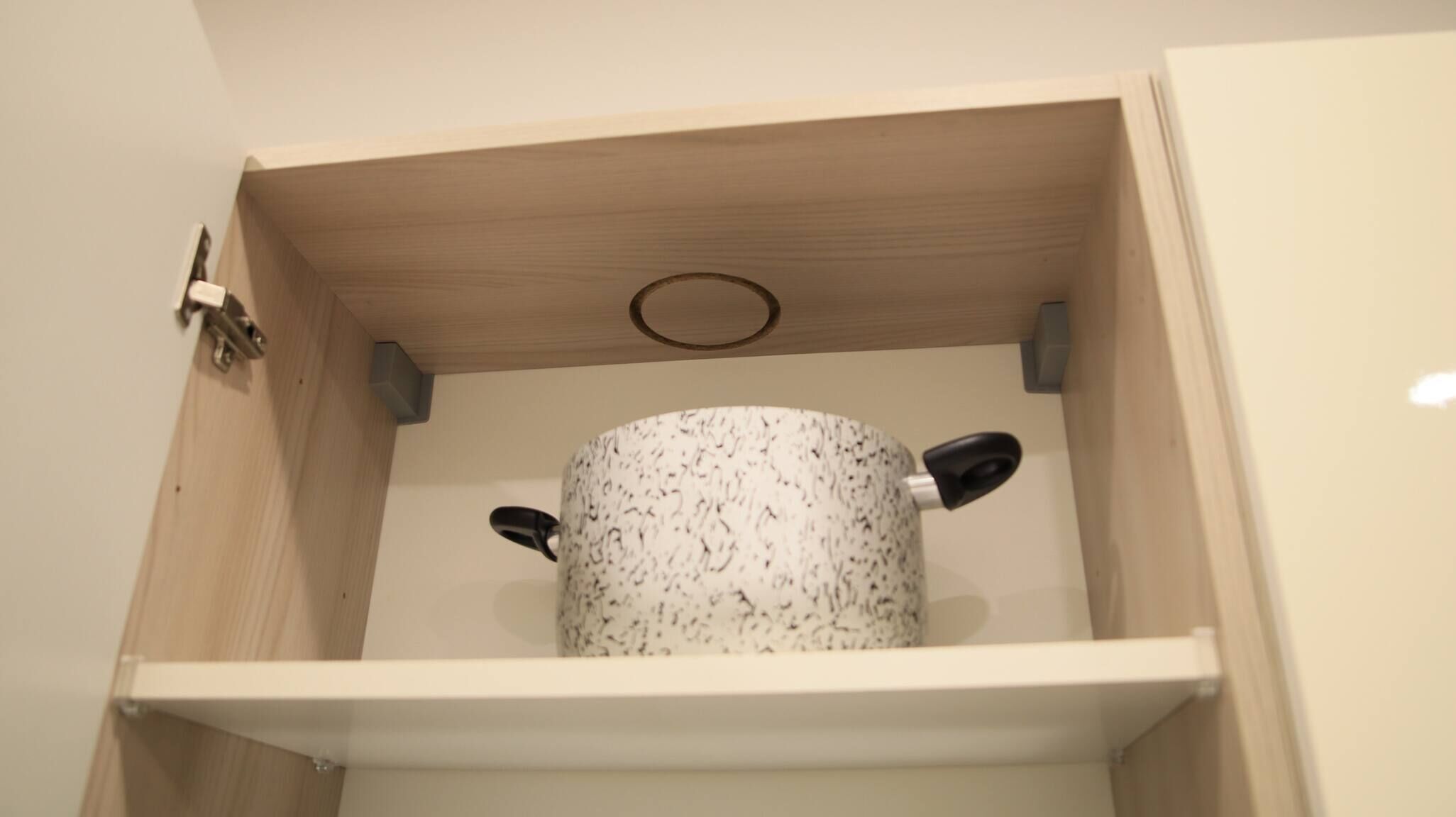 A wooden cabinet with a white interior, containing a white object with black handles.
