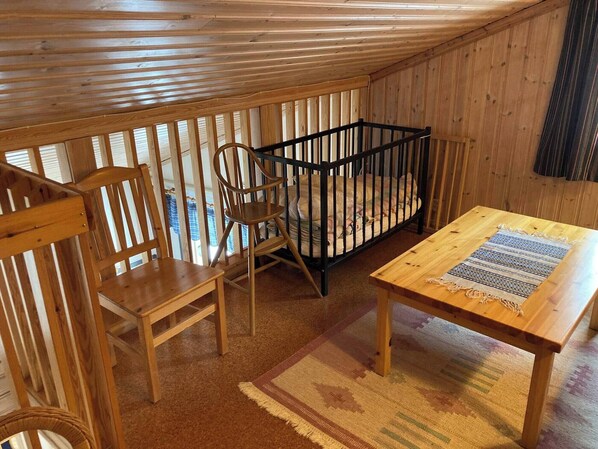 A cozy room with wooden walls and a sloped ceiling. There is a crib, a wooden table, and two chairs.