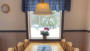 A dining room with a wooden table, chairs, a hanging lamp, a clock, and a window with a view of trees. - beautiful mountains in Sälen högfjället Sweden (Sälen)