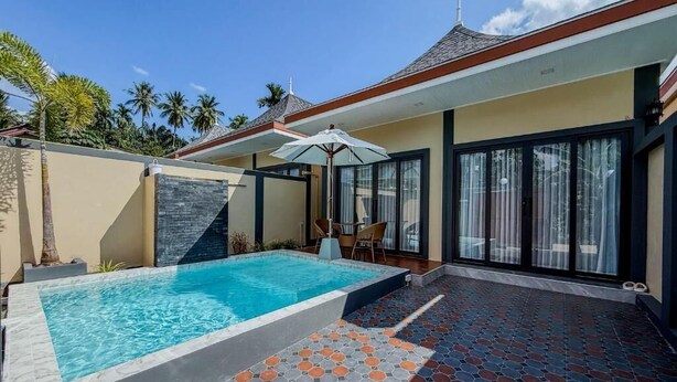 Une maison moderne dotée d’une piscine, d’un patio aux carreaux décoratifs et d’une porte vitrée donnant sur un espace extérieur abrité.