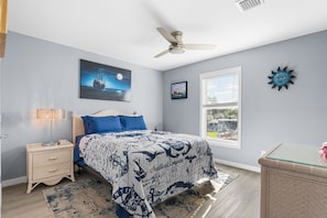 A bedroom with a bed, a nightstand, a ceiling fan, a window with blinds, and a wall-mounted sun decoration. - Amazing little fishing cabin on the water with a boat ramp in Everglades City (Everglades City)