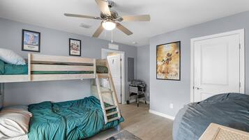 Una habitación con literas, ventilador de techo, escritorio y puerta.