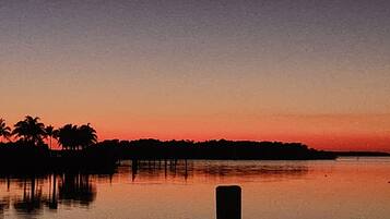 A sunset over a calm body of water with palm trees silhouetted against the sky.